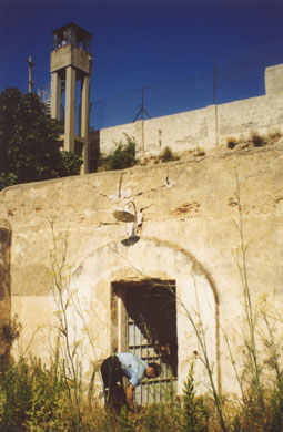 Un agente apre il cancello che porta a un piccolo cortile quadrato che precede l'area delle celle della "polveriera grande". In alto il muro di cinta del carcere ancora in funzione, con l'altissima torretta.